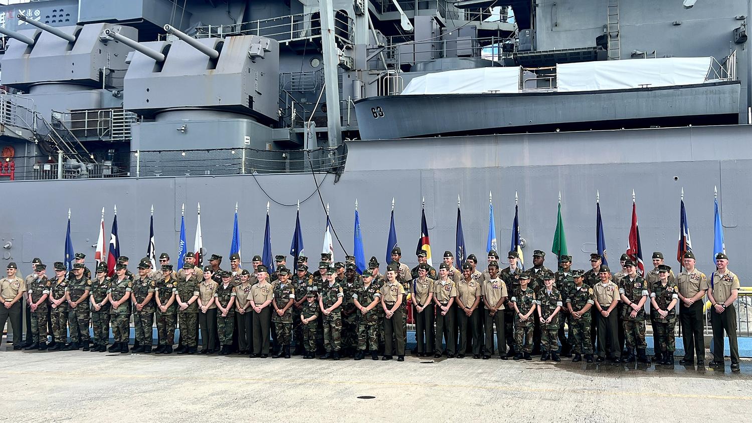 Young Marines assembled with state flags alongside a battleship at Pearl Harbor